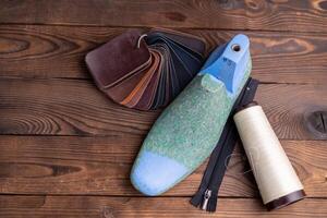 Leather samples for shoes and wooden shoe last on dark wooden table. photo