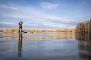 senior paddler and his paddleboard on lake in winter or early spring in Colorado, frog perpective, partially submerged action camera photo