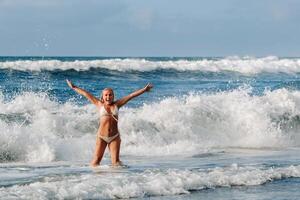 un niña con mojado pelo felizmente nada en el olas en el atlántico océano.tenerife.españa foto