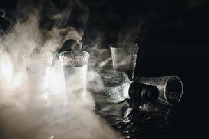 Vodka in shot glasses on black background, iced strong drink in misted glass. photo