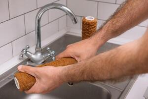 Hand holding dirty water filter cartridge over the sink. Brown coloring. Evidence of contamination of tap water with iron cations. photo