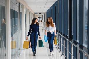 Two girl-friends on shopping walk on shopping centre with bags photo