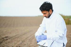 Soil Test. Indian Agronomist putting soil with garden shovel in soil sample bag outdoor. Environmental research photo