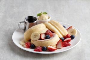 Kiseki Pancake with Fresh Fruits banana, strawberry, raspberry and Maple Butter Cream in white plate on grey background photo