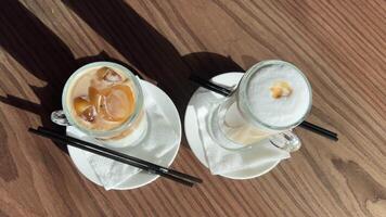 latté dos tipos frío y caliente hielo latté y clásico en de madera mesa, Leche y café servicio comparación elección verano y invierno preferencia de cerca dos lentes con negro pajitas en cafetería. bebida capas video