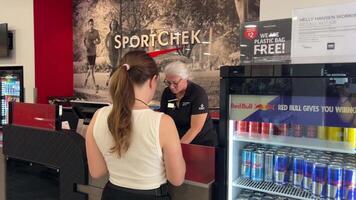 SportChek a young teenage girl with ponytail very happily buys herself a new pink glamorous cap in an expensive sports store near the machine with Red Bull Canada 2023 video