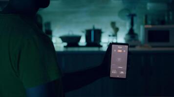 maschio Tenere mobile con illuminazione controllo App seduta nel cucina di Casa con automazione leggero sistema, svolta su lampadina. smartphone per Casa automazione sistema, alto Tech applicazione per inteligente casa video