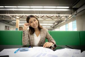 Beautiful asian businesswoman is shown thinking in the copy space with a smile with papers on her desk photo