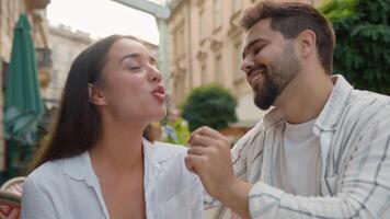 Boyfriend feeding girlfriend European couple lovers kissing sweet kiss love feelings relationship smile laugh Caucasian woman and man hugging eat in city cafe romantic date outdoors romance tenderness video