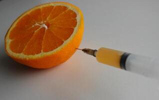 Vitamins content in fruits illustration. Orange juice fills a syringe, the needle of which is inserted into the half of the juicy orange through the peel photo