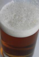 vertical foto de un alto paredes delgadas cerveza vaso con clásico espuma en pálido cerveza inglesa