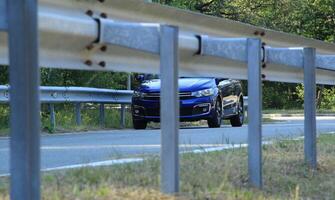 Metal railing in front of blue sedan on the asphalt road photo