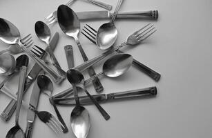 Variety size spoons, forks and table knives scattered on white surface at a side of image photo