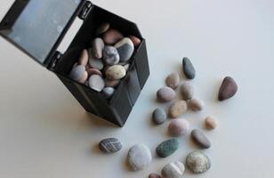 Black container mockup with colored pebbles inside and scattered pebbles near it on white surface photo