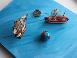 A board painted with an ocean pattern with models of sailing ships, a globe and a compass on it photo