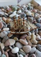 Vertical Concept Photo On Topic Of Sea Travel. Toy Sailing Vessel In Box Filled With Sea Rocks