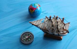 Sea Travel Concept Image. Globe, Wooden Ship Model And Vintage Compass On Blue Surface Symbolizing Ocean photo