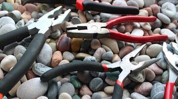 Variety types of pliers with rubberized handles laid out on a sea stones angle view photo