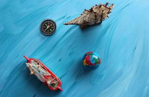 Miniatures on the theme of sea travel. Compass And Small Globe Near Sailing Ships Model On Blue Painted Surface photo