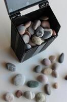 Construction And Decoration Materials. Scattered Pebbles And Black Plastic Container Full Of Smooth Pebbles On A Clean White Surface photo