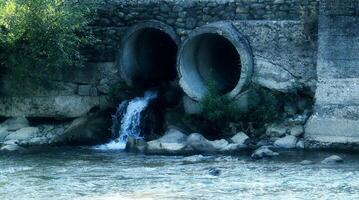 Contaminated water from the canalization pipes pollutes clear river photo