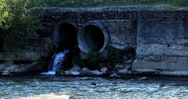 Liquid effluent falling in natural river water from sewage pipes photo