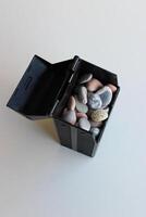 Opened Lid Of Black Box With Colored Sea Stones On White Surface Vertical Stock Photo
