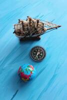 Top View Of Wooden Sailing Ship Mockup, Compass And Globe On Painted Sea Surface Vertical Stock Photo