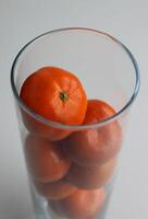 Fresco naranja mandarinas en un Delgado vaso florero en blanco superficie foto