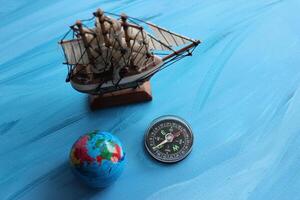 Circle Compass With Blurred Masted Ship Model And Small Globe Around On Blue Surface With Painted Waves photo