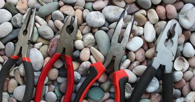 Top parts of variety types of pliers lined up in size comparison on a round smooth rocks concept photo for background or wallpapers