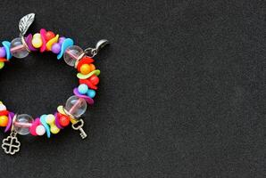 Concept For Postcard Or Invitation. Bracelet With Colorful Beads And Silver Charms In A Side Of Image On Black Background photo