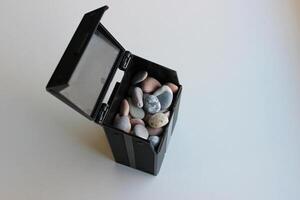 Construction And Decoration Materials. Black Plastic Container Mockup Full Of Smooth Pebbles On A Clean White Surface photo