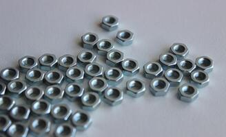 Many same iron nuts are tightly fitted to each other in an abstract shape on a white table photo