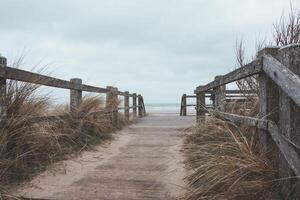 Entrada a el arenoso playa a Blankenberge. un de madera muelle debajo un pesado lluvioso cielo foto