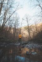 Young man in an orange jacket relaxes in the flow of a river in the Wallonia region of Belgium. Reflection of a man in the river water. Discovering wildlife in Belgium photo