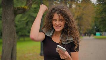 Happy amazed excited surprised woman Caucasian girl hold mobile phone reading news win celebrate victory fortune with smartphone shock yes success happy celebrating after sport outdoors in city park video