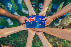 Group of people displaying New Zealand flag with hands in grassy field photo