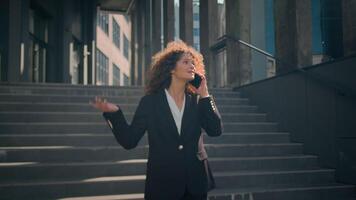 Kaukasisch zakenvrouw jong vrouw meisje bedrijf dame manager ondernemer baas wandelen van kantoor gebouw pratend cel telefoon buitenshuis ontevreden geërgerd vrouw ruzie maken mobiel telefoontje in stad buitenshuis video