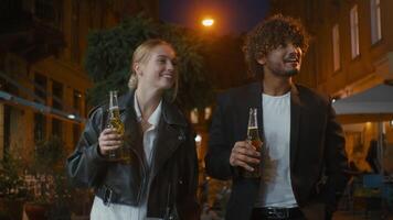 dos mejor amigos mujer y indio hombre caminar ciudad calle noche bebida sidra cerveza comunicar hablar juntos Pareja pasatiempo risa disfrutar que se discute fin de semana conversacion charla hablar sonriente celebrar enlace video