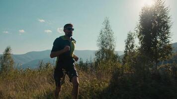 athlétique caucasien homme Masculin gars tenue de sport des lunettes de soleil coureur promeneur fonctionnement vallée randonnée courir en mouvement escalade en haut Montagne exercice vert colline en plein air aventure sport en bonne santé mode de vie actif faire des exercices video