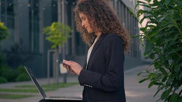 caucasico ragazza datore di lavoro Amministratore delegato chat smartphone all'aperto nel città centro attività commerciale donna lettura notizia mobile Telefono aggeggio Lavorando su il computer portatile computer rendere in linea ordine femmina giovane donna d'affari opera video