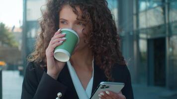 Close up Caucasian woman smiling businesswoman female walking drinking coffee in city happy cheerful business girl hold smartphone scrolling social media online chatting mobile phone drink go outdoors video