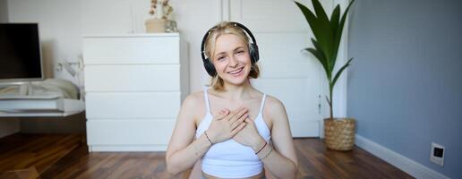 Portrait of young happy woman in headphones, looking with relaxed, friendly face expression, holding hands on her chest and smiling photo