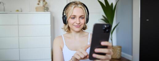 Close up portrait of smiling sporty woman, wearing headphones, using mobile phone, workout app while exercising at home photo