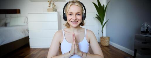 Wellbeing and people concept. Close up portrait of young woman in headphones, meditating, practice yoga, listens to podcast in earphones photo