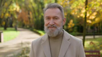Portrait senior Caucasian male intelligent 60s old man happy retired bearded grandpa in city park satisfied joyful middle age gentleman looking at camera happiness emotion smile outdoors autumn nature video