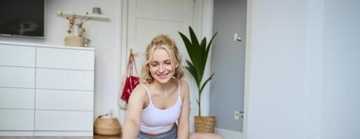 Portrait of young fitness instructor, vlogger creating content at home, doing workout and record exercises on digital camera, using rubber yoga mat photo