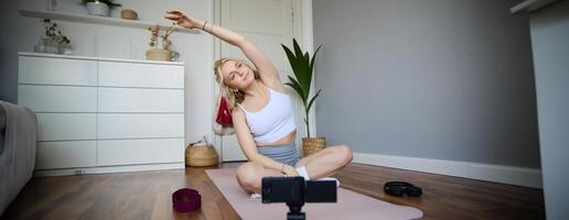 Portrait of young blogger, yoga content creator, showing exercises, recording of herself working out at home on rubber mat photo