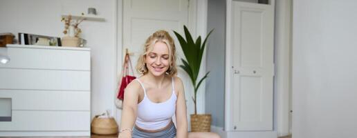 Vertical shot of woman recording her workout on digital camera, making a about yoga and fitness at home, sitting on rubber mat in activewear photo